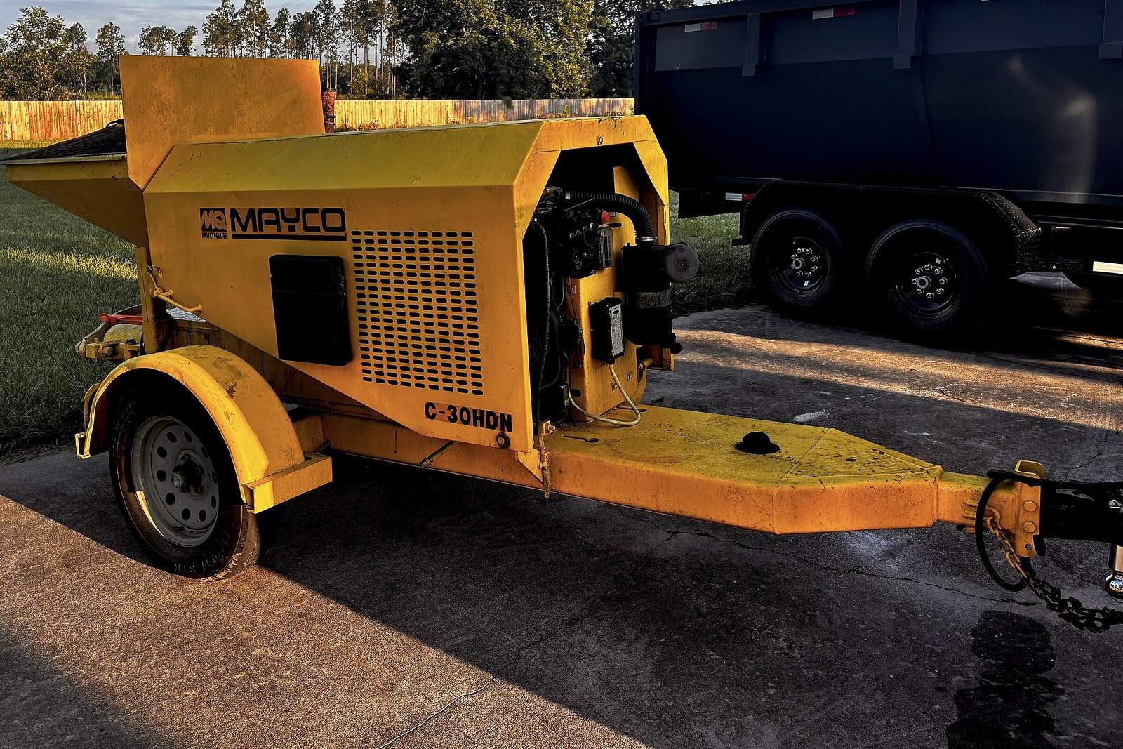 Bomba de concreto Mayco C-30HDN amarilla montada en trailer, estacionada en una entrada de concreto a la luz del atardecer.
